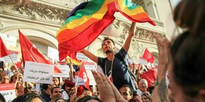 Ein Man schwenkt auf einer Demonstration die Regenbogenflagge