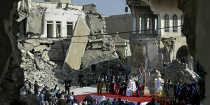 Papst thront auf roten Teppich in den Ruinen einer Kirche.