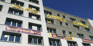 Eine graue Hausfassade, mehrerer Banner hängen aus den Fenstern. "Deutsche Wohnen und Co enteignen" ist auf ihnen zu lesen - wobei ein schwarzes "zensiert"-Plakat über dem mittleren Banner gehängt wurde.
