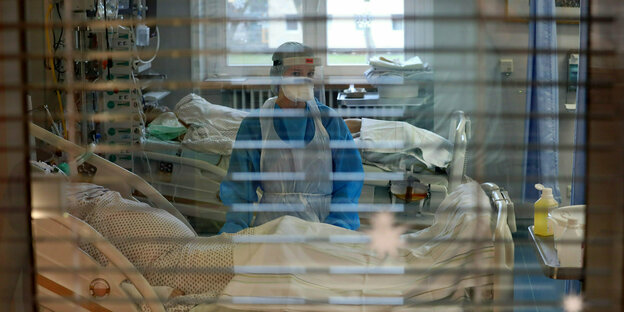 Eine Pflegekraft steht hinter Jalousien im Infektionszimmer für Covid-19-Patienten
