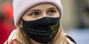 Eine Aktivistin steht am „Internationalen Tag gegen Gewalt an Frauen“ vor dem Brandenburger Tor und trägt einen Mund-Nasen-Schutz mit der Aufschrift „Frei leben - Ohne Gewalt“.