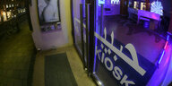 In blauem und rotem Licht leuchtet der Innenraum des Habibi Kiosk der Münchner Kammerspiele in der Maximilianstrasse, auf der eine Trambahn fährt.