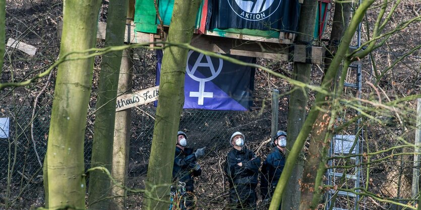 Polizist:innen stehen im Wald unter einem Baumhaus und gucken hoch