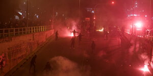 Demonstrierende zünden rote Leuchtfackeln nachts iun den Straßen von Athen