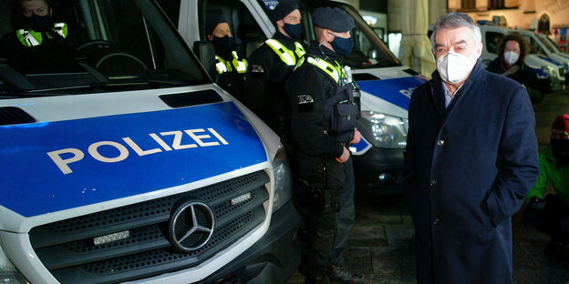 NRW-Innenminister Herbert Reul vor zwei Polizeiautos samt Beamten
