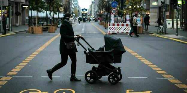 Eine Passantin mit Kinderwagen ueberquert einen Radweg