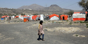 Ein Mädchen läuft vor einem Flüchtlicngscamp in karger Landschaft