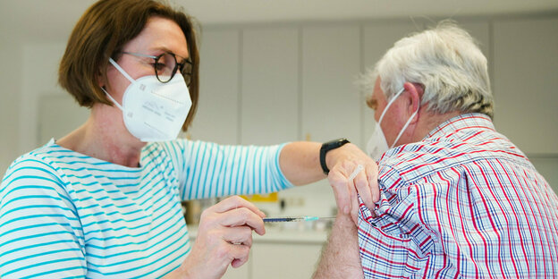 Ärztin mit Mundschutz sticht Spritze in den Arm eines abgewandten weißhaaruigen Mannes