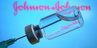 Impfstoff in Ampulle und Spritze - Herstellerlogo Johnson & Johnson im Hintergrund