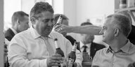 Schwarz weiß Bild zwei Männer stoßen mit Bier an, im Hintergrund sind weitere zu sehen