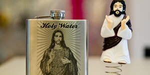Ein Flachmann mit Jesus darauf und der Inschrift "Holy Water", daneben eine Jesusfigur