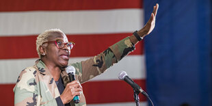 Nina Turner - schwarze Frau mit blond gefärbten kurzen Haaren gestikuliert vor USA Flagge