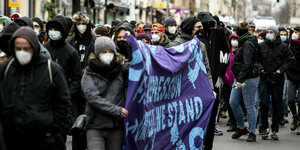 Viele Menschen mit Masken bei einer Demo, einige halten ein lila Transparent mit hellblauen Schriftzeichen