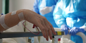 Die Hand einer an Covid-19 erkrankten Person währen einer Visite im Krankenhaus