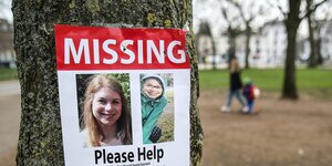 Ein Suchplakat mit der Aufschrift "Missing" und zwei Portraitfotos einer Frau hängt an einem Baumstamm