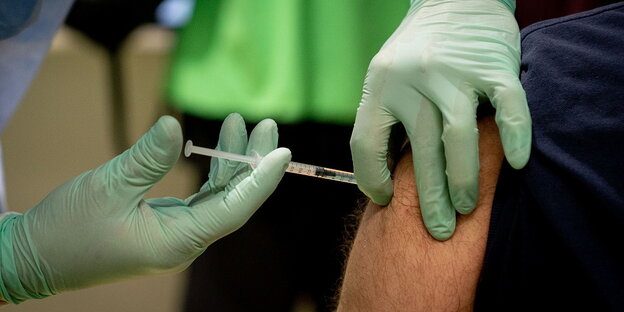 Ein Arzt mit grünen Schutzhandschuhen impft einen Menschen, Detailaufnahme