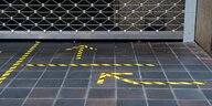 Schwarz-gelbe Markierungen auf dem Fußboden vor einem geschlossenem Ladengeschäft, Detailaufnahme
