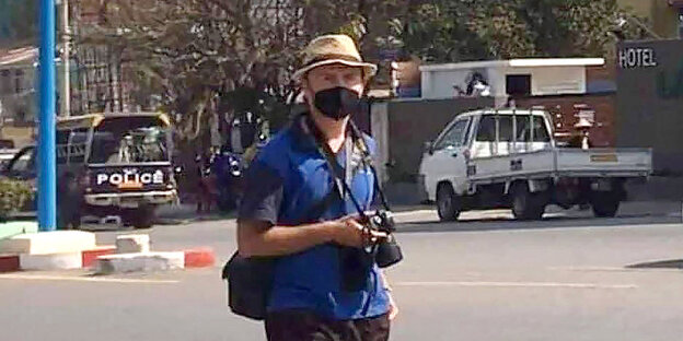 Ein Journalist mit Mundschutz und einer Kamera in den Händen steht auf einer Straße