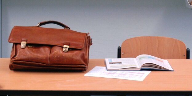 Eine Aktentasche und ein aufgeschlagenes Buch liegen auf einem Tisch