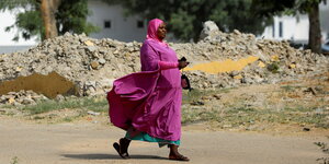 Eine Frau in einem pinkfarbene Kleid und Kopftuch geht eine Straße entlang