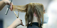 Eine Friseurin schneidet einer Frau mit Mundschutzmaske die Haare