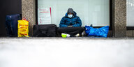 Ein Obdachloser sitzt vor einer Ladenzeile