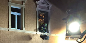 Ein Feuerwehrmann schaut aus einem ausgebranntem Fenster