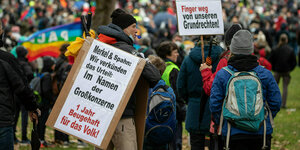 Ein Mann auf einer Demo trägt ein Plakat mit der Aufschrift: "Merkel&Spahn: Wir verkünden das Urteil: Im Namen der Großkonzerne 1 Jahr Beugehaft für das Volk