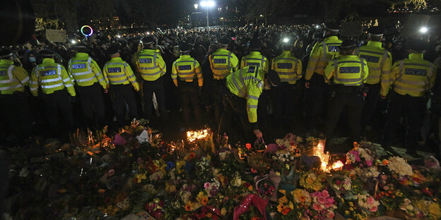 Eine Reihe PolizeibeamtInnen steht vor einem Meer aus Blumen.Dahinter eine Menschenmenge