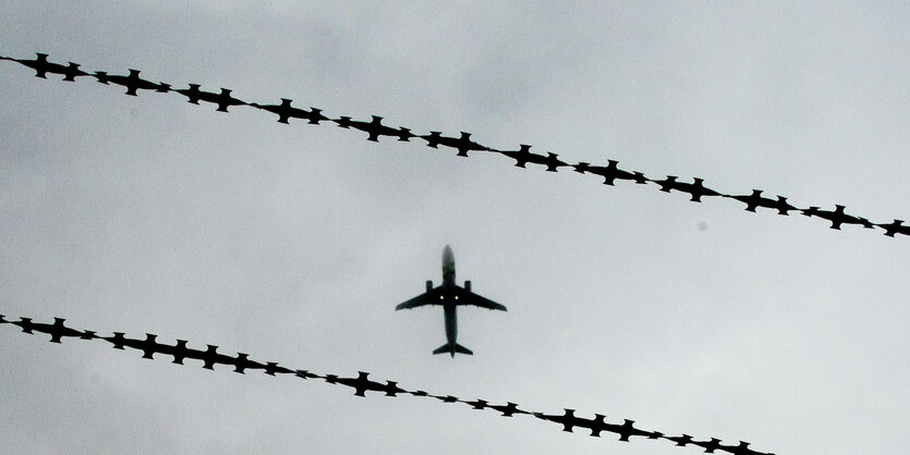 Ein fliegendes Flugzeug ist hinter Stacheldraht zu sehen