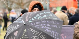 Ein Demonstrant hät einen schwarzen Schirm mit aufgekritzelten Parolen in die Kamera