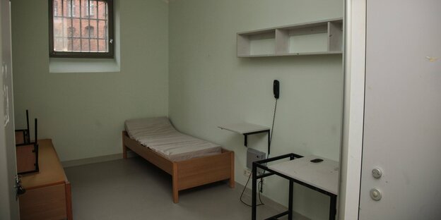 Gefängniszelle mit vergittertem Fenster, zwei Einzelbetten, Regal, Tisch und Telefon