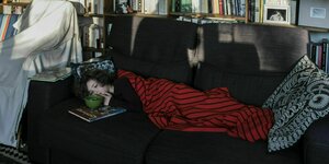 ein kind liegt in einem Wohnzimmer mit Gefülltem Bücjerregal auf der Couch.