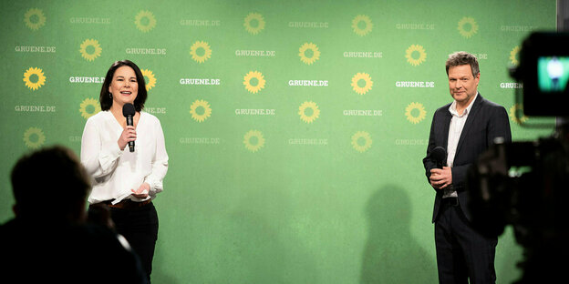 Annalena Baerbock und robert Habeck stehen vor einer grünen Wand mit Sonnenblumen