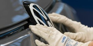 Hände in Gummihandschuhen polieren VW-signet an einer Motorhaube
