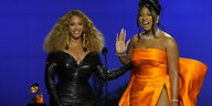 Beyonce und die Rapperin Megan Thee Stallion tragen schwarze und orangene Kleider und lächeln