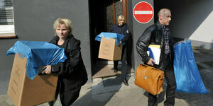 Zwei Frauen und ein Mann tragen Pappkartons aus der Haustür. Auf den Pappkartons steht BKA Tatortgruppe