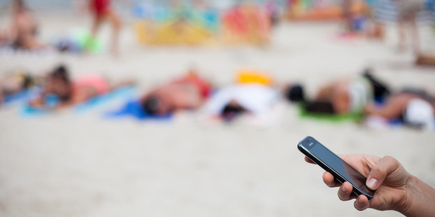 Am Strand hält eine Person ein Smartphone in der Hand.