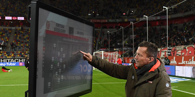 Lothar Matthäus deutet auf einen großen TV-Bildschirm