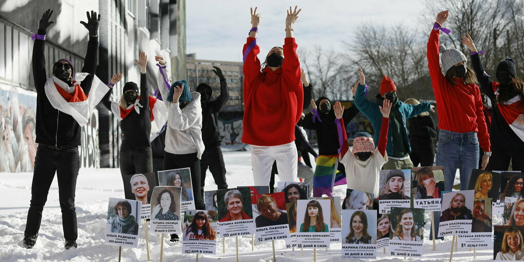 Demonstrierende in Minsk strecken ihre Arme in die Luft - vor ihnen Fotos von inhaftierten oppostionellen Frauen