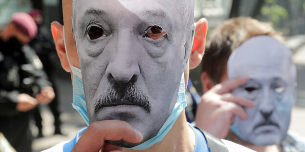 Zwei Männer halten sich schwarz weiß Masken des belarussischen Präsidenten Alexander Lukaschenko vors Gesicht
