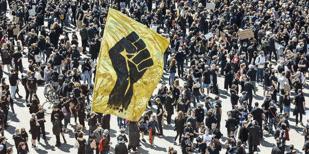 Protest auf dem Alexanderplatz mit vielen Menschen und gelber Fahne mit einer Schwarzen, geballten Faust