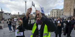 Demonstration - im Voderdergrund ein Mann mit gelber Warnweste, Mundschutz - er schlägt Löffel und Gabel zusammen