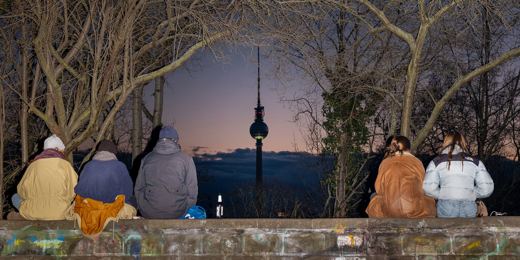 Menschen sitze auf einer Mauer vor der Kulisse des Fernsehturms