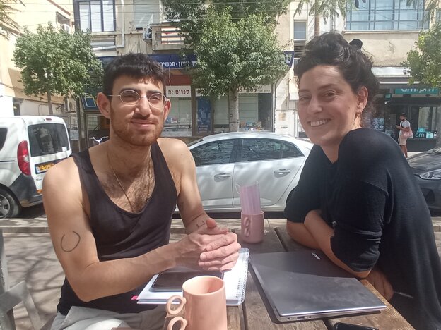ein unger Mann und eine junge Frau sitzen draussen an einem Holztisch in Tel Aviv ein unger Mann und eine junge Frau sitzen draussen an einem Holztisch in Tel Aviv