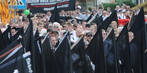Eine Gruppe von Männer demonstriert mit schwarzen Fahnen und Bannern
