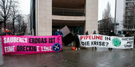 Klimaaktivist*innen protestieren mit Bannern vor einem Gebäude