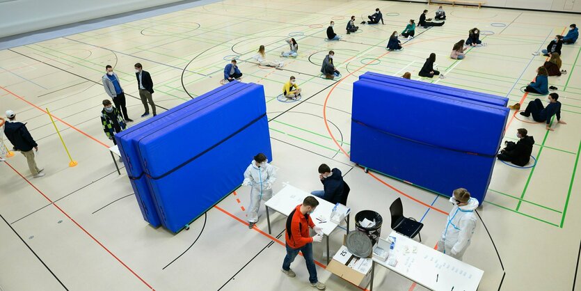 SchülerInnen hocken auf dem Boden einer Turnhalle und warten auf ihre Testung