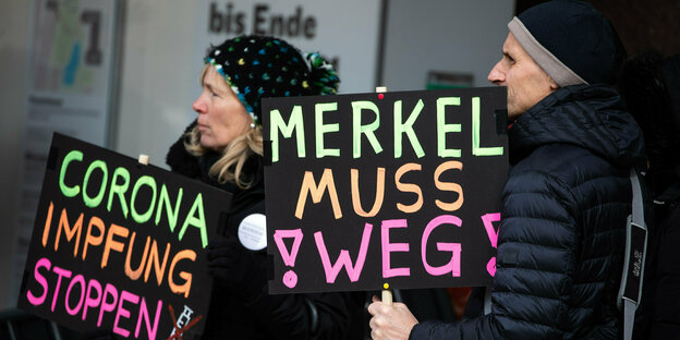 Ein Frau und Mann bei der Demo. Auf ihren Schildern steht: "Merkel muss weg" und "Corona Impfung stoppen"