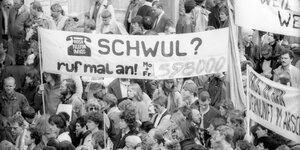 Schwarz-weiß Foto einer Demo. Auf dem Banner steht: Schwul? Ruf mal an.